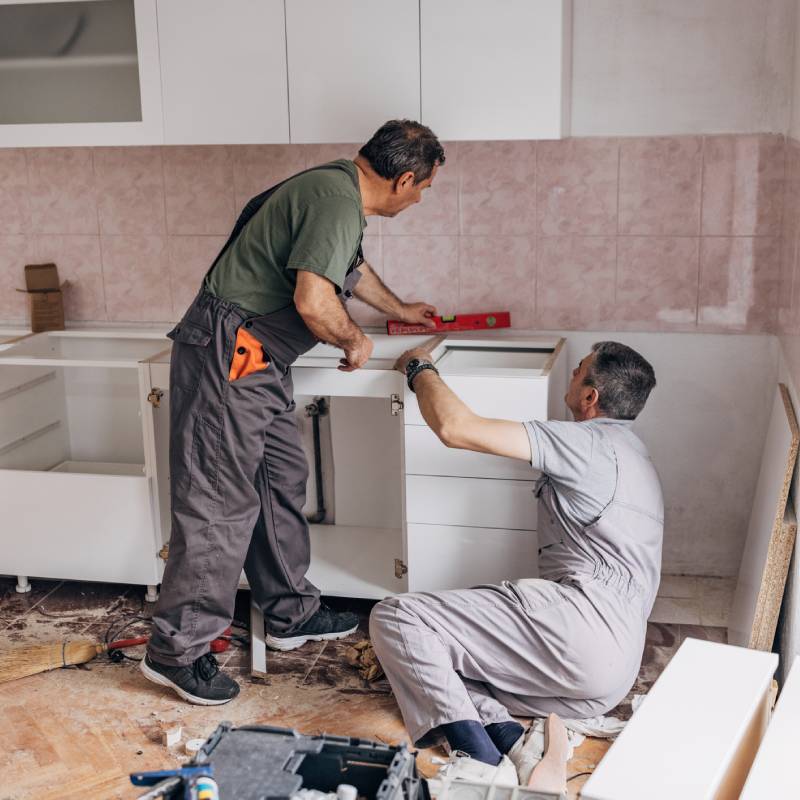 Two workers installing kitchen cabinets in a modern home.