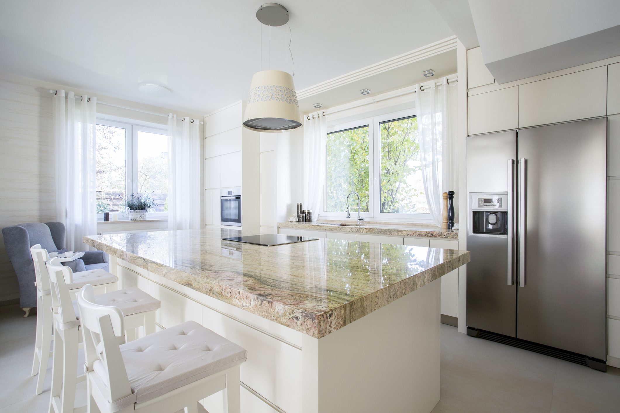 Bright modern kitchen with marble island and white stools.